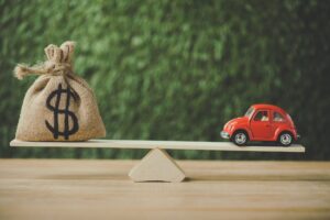 toy car and money bag with dollar sign balancing on seesaw on green background